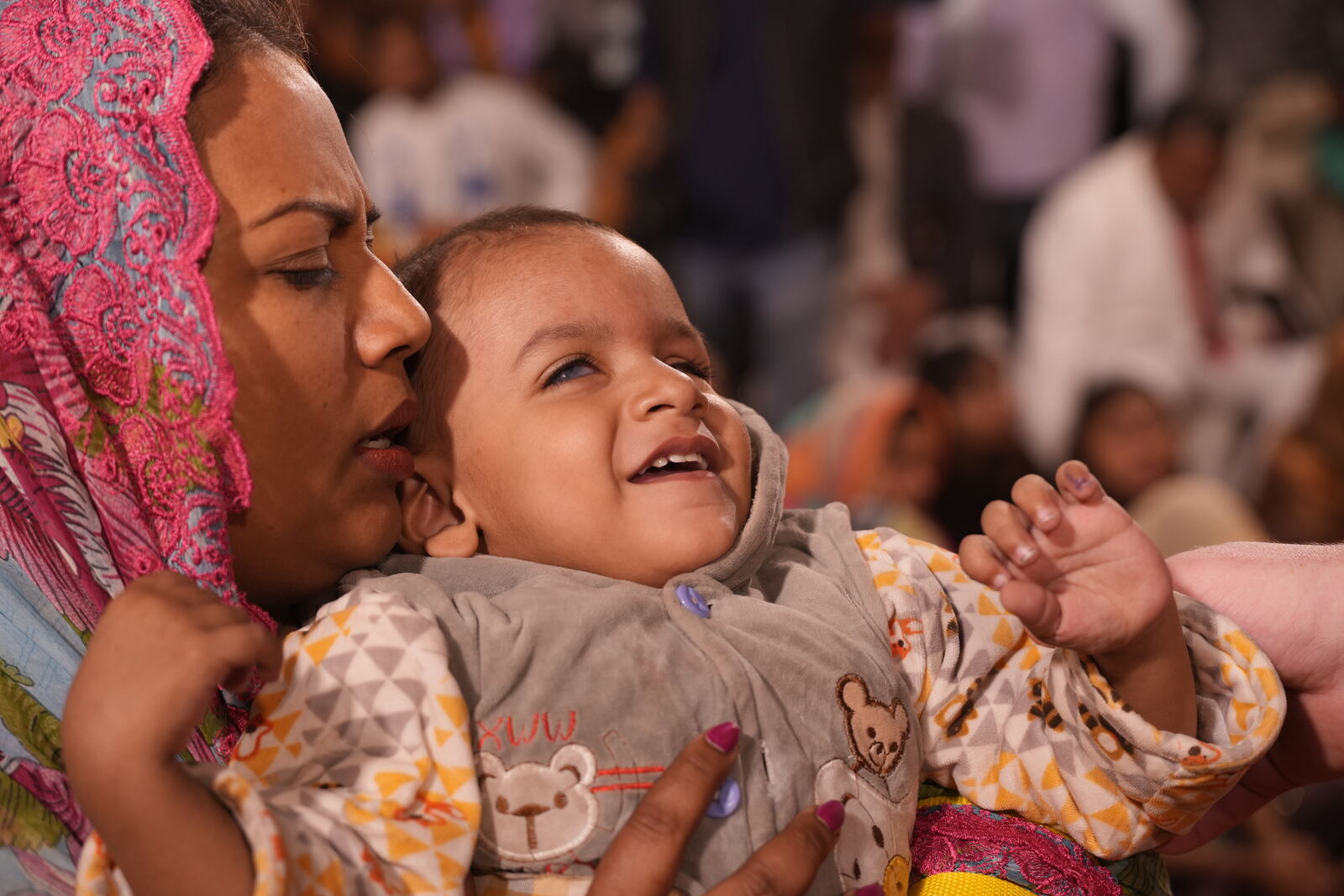 The same baby laughing in his mother's arms after prayer