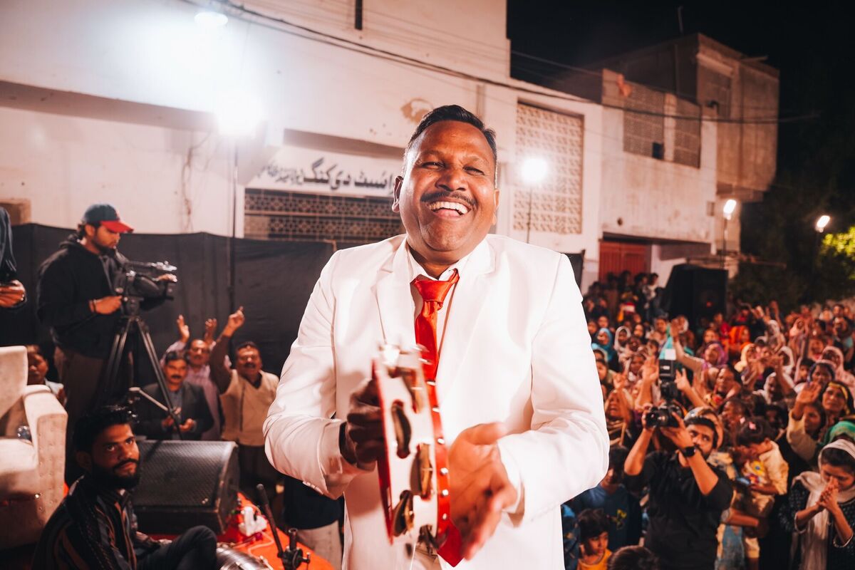A pastor in a white suit laughing with a tambourine